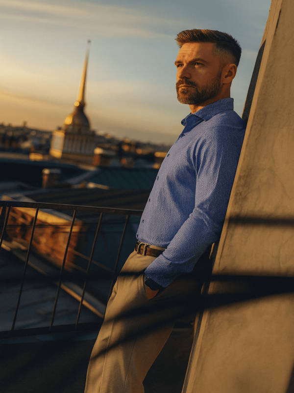 Man in a blue shirt standing on a rooftop with a cityscape background