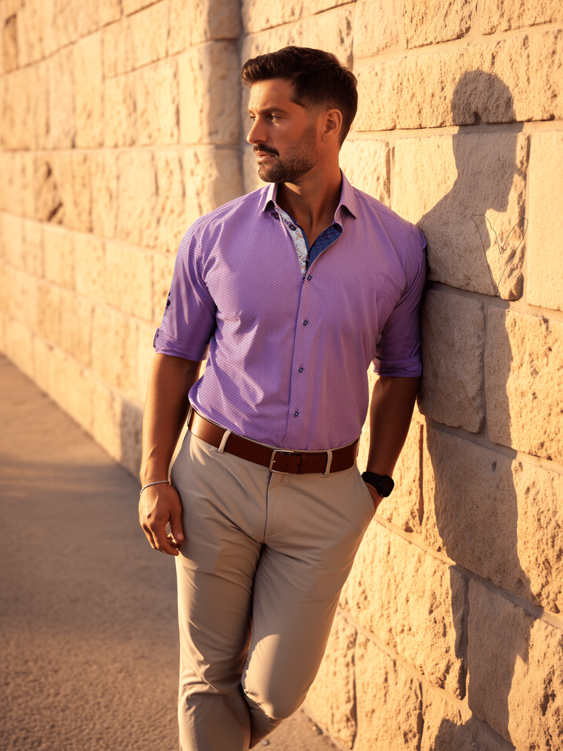 Man in a purple shirt and beige pants leaning against a stone wall.